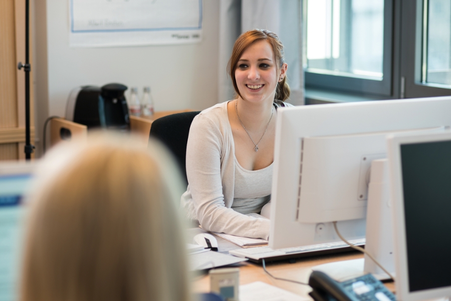 Junge Frau sitzt an einem Computerarbeitspaltz und lächelt