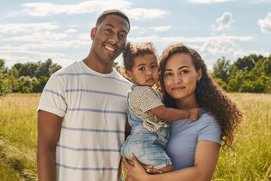 Junge dreiköpfige Familie steht auf einem Feld in der Sommmersonne Junge dreiköpfige Familie steht auf einem Feld in der Sommmersonne
