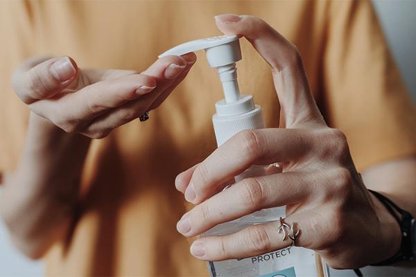 Hand hält Desinfektionsmittelflasche und gibt etwas davon auf die andere Hand Hand hält Desinfektionsmittelflasche und gibt etwas davon auf die andere Hand
