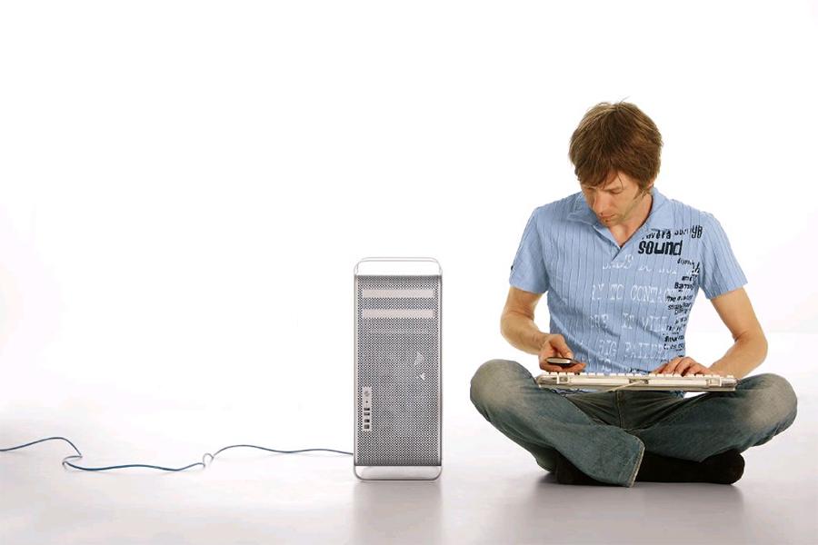 Foto: Ein Mann sitzt im Schneidersitz neben einem Rechner, die Tastatur auf seinem Schoß und sein Handy in der Hand