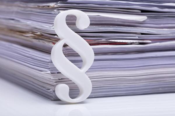 Foto: Paragrephenzeichenlehnt an einem Aktenstapel Foto: Paragrephenzeichenlehnt an einem Aktenstapel