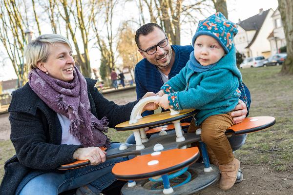 Eltern spielen mit ihrem kleinen Sohn auf der Federwippe auf dem Spielplatz