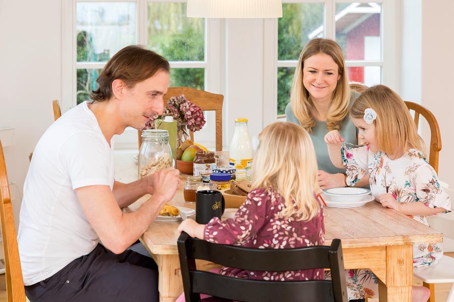 Vater und Mutter sitzen zusammen mit ihren kleinen Töchtern am Frühstückstisch