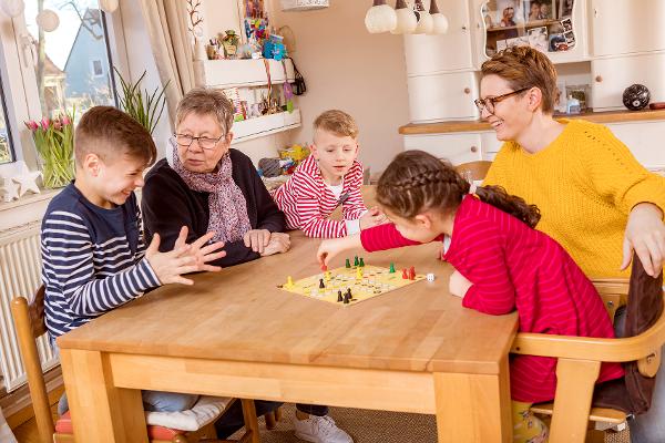 Eine Großmutter spielt zusammen mit ihren Enkelkindern und Tochter das Spiel "Mensch ärgere dich nicht"