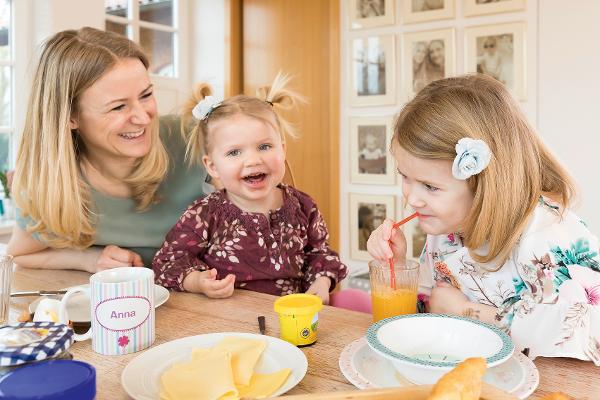 Eine Mutter lacht mit ihren beiden Töchtern zusammen am Frühstückstisch