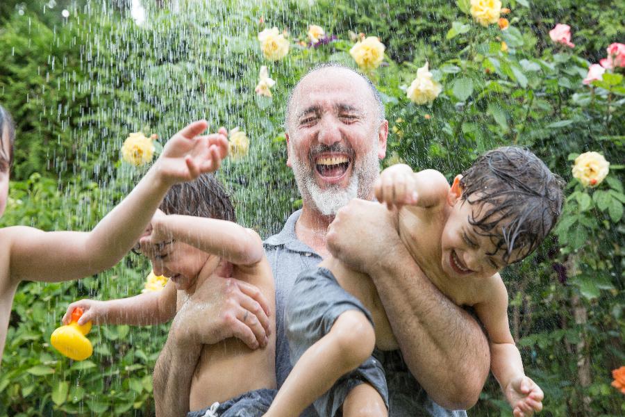 Ein Vater spielt mit seinen Söhnen unter einem Wasserstrahl Ein Vater spielt mit seinen Söhnen unter einem Wasserstrahl
