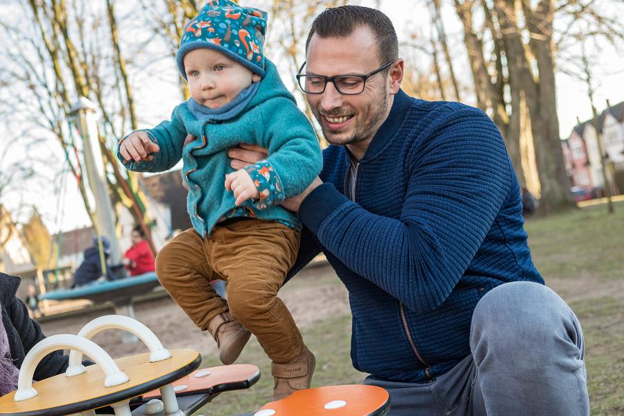 Ein Vater spielt mit seinem Sohn auf einer Federwippe auf dem Spielplatz Ein Vater spielt mit seinem Sohn auf einer Federwippe auf dem Spielplatz