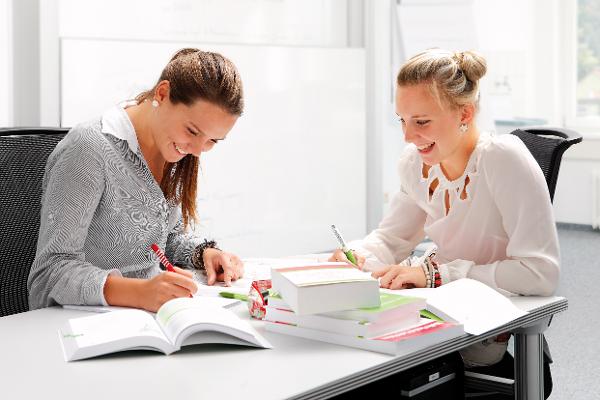 Zwei junge Frauen sitzen an einem Tisch, auf dem mehrere Bücher liegen. Zwei junge Frauen sitzen an einem Tisch, auf dem mehrere Bücher liegen.