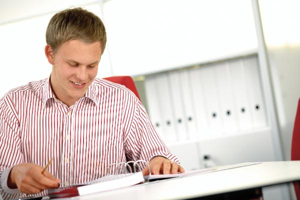 Ein junger Mann sitzt an einem Tisch und liest in einem Aktenordner. Ein junger Mann sitzt an einem Tisch und liest in einem Aktenordner.