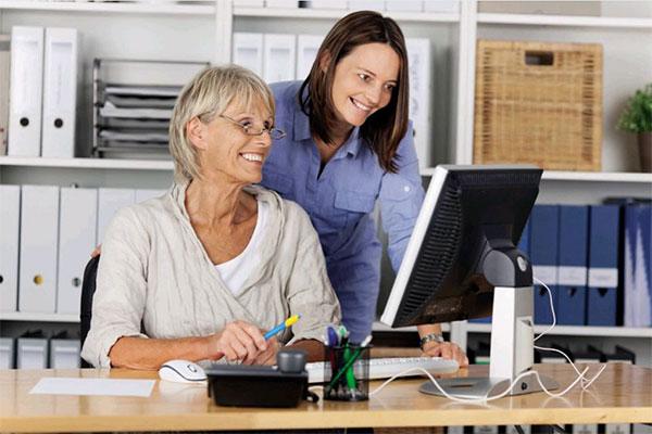Zwei Damen am Schreibtisch schauen lachend auf einen Monitor Zwei Damen am Schreibtisch schauen lachend auf einen Monitor