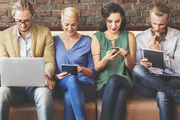 Vier junge Menschen auf einer Bank blicken auf verschiedene digitale Endgeräte Vier junge Menschen auf einer Bank blicken auf verschiedene digitale Endgeräte