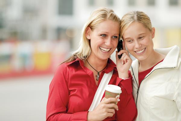 Zwei junge Frauen halten ihre Ohren an einem Handy