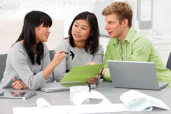 Drei junge Menschen sitzen an einem Tisch und unterhalten sich, vor ihnen stehen Laptops. Drei junge Menschen sitzen an einem Tisch und unterhalten sich, vor ihnen stehen Laptops.