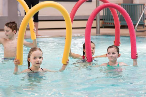 Eine Gruppe von Kindern beim Schwimmtraining mit Schwimmnudeln Eine Gruppe von Kindern beim Schwimmtraining mit Schwimmnudeln