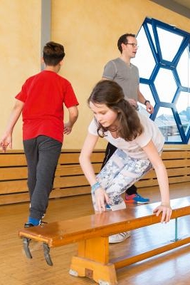 Eine Gruppe von Kindern trainiert auf einer Turnbank und wird von einem Trainer betreut. Eine Gruppe von Kindern trainiert auf einer Turnbank und wird von einem Trainer betreut.