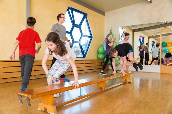 Eine Gruppe von Kindern trainiert auf einer Turnbank und wird von einem Trainer betreut Eine Gruppe von Kindern trainiert auf einer Turnbank und wird von einem Trainer betreut