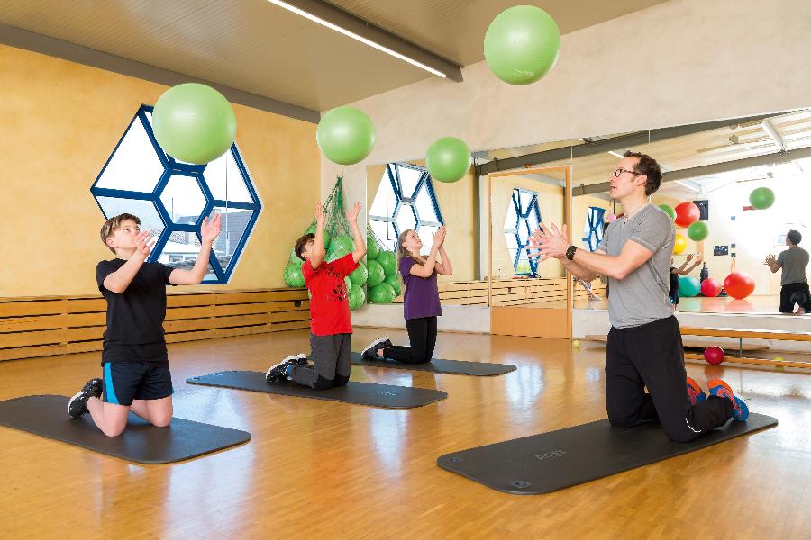 Eine Gruppe von Kindern trainiert mit Gymnastikbällen und wird von einem Trainer betreut Eine Gruppe von Kindern trainiert mit Gymnastikbällen und wird von einem Trainer betreut