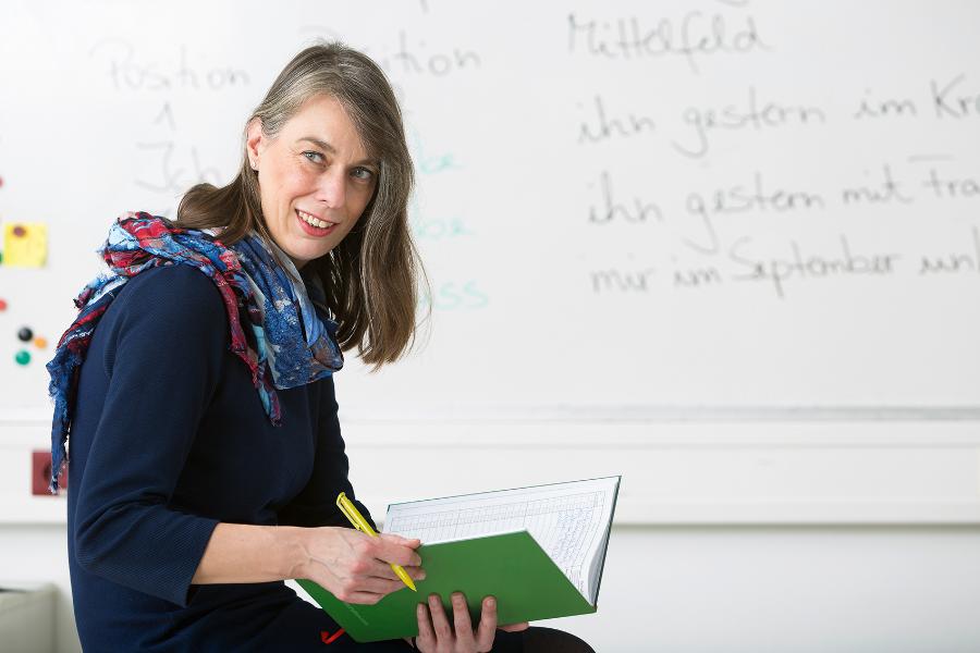 Eine Lehrerin sitzt vor der Tafel und schreibt in das Lehrerbuch Eine Lehrerin sitzt vor der Tafel und schreibt in das Lehrerbuch