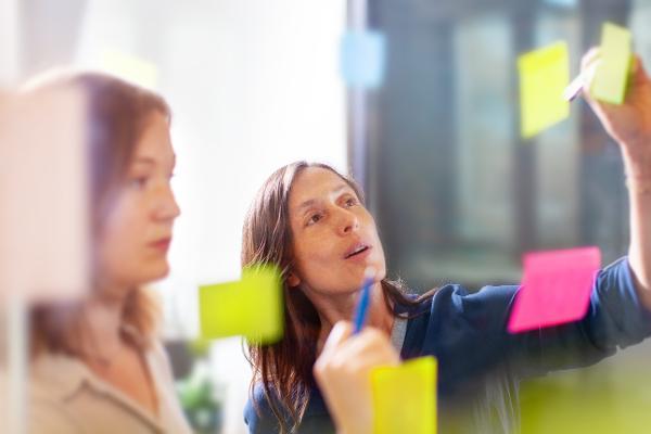 Kollegen kleben Post-its an eine Glaswand Kollegen kleben Post-its an eine Glaswand