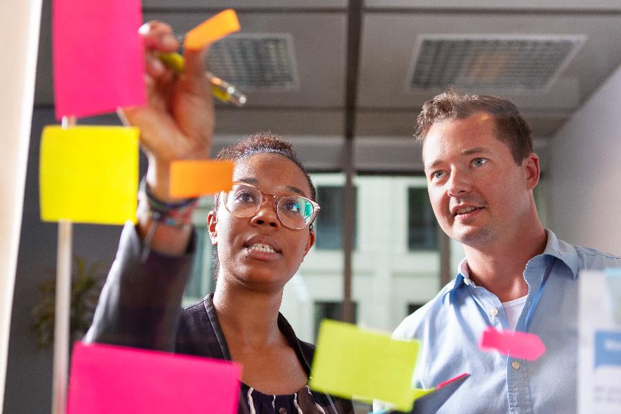 Kollegen kleben Post-its an eine Glaswand Kollegen kleben Post-its an eine Glaswand