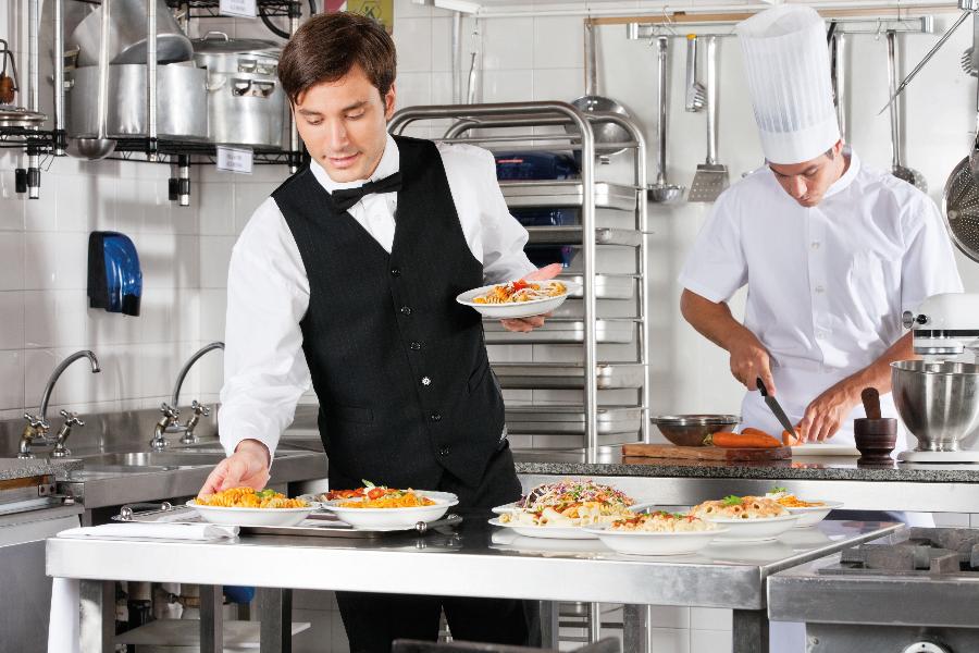 Ein Kellner trägt Teller mit Essen aus einer Küche.