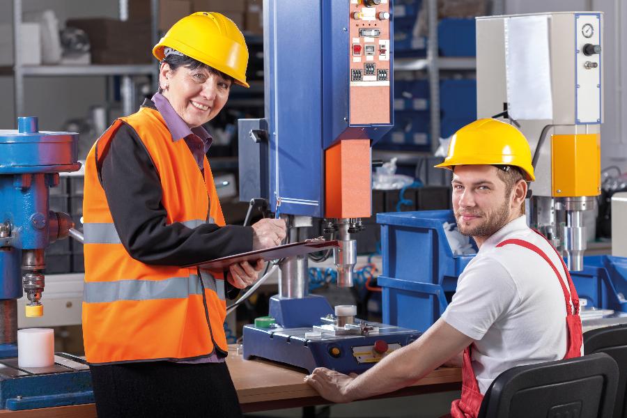 Eine Prüferin und ein Arbeiter sind an einer industriellen Maschine tätig Eine Prüferin und ein Arbeiter sind an einer industriellen Maschine tätig