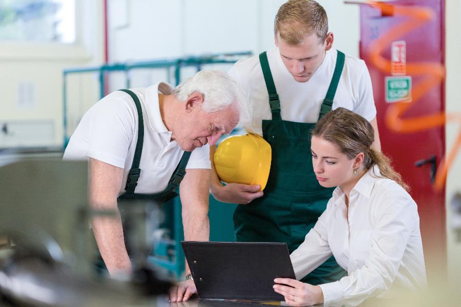 Zwei Industriearbeiter werden von einer Kollegin eingewiesen