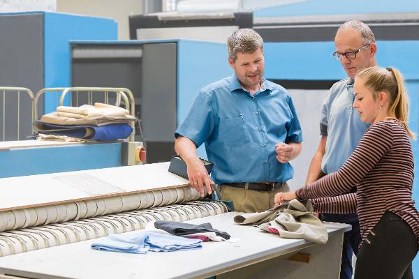 Drei Mitarbeiter einer Textilfabrik schauen sich Stoffzuschnitte an. Drei Mitarbeiter einer Textilfabrik schauen sich Stoffzuschnitte an.