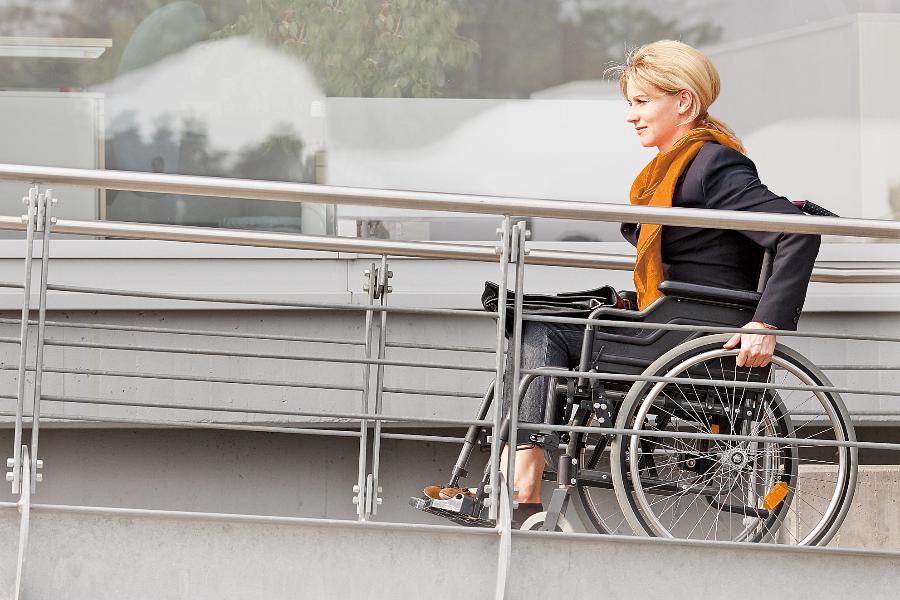 Eine Frau mittleren Alters bewegt sich in ihrem Rollstuhl eine Rampe hoch Eine Frau mittleren Alters bewegt sich in ihrem Rollstuhl eine Rampe hoch