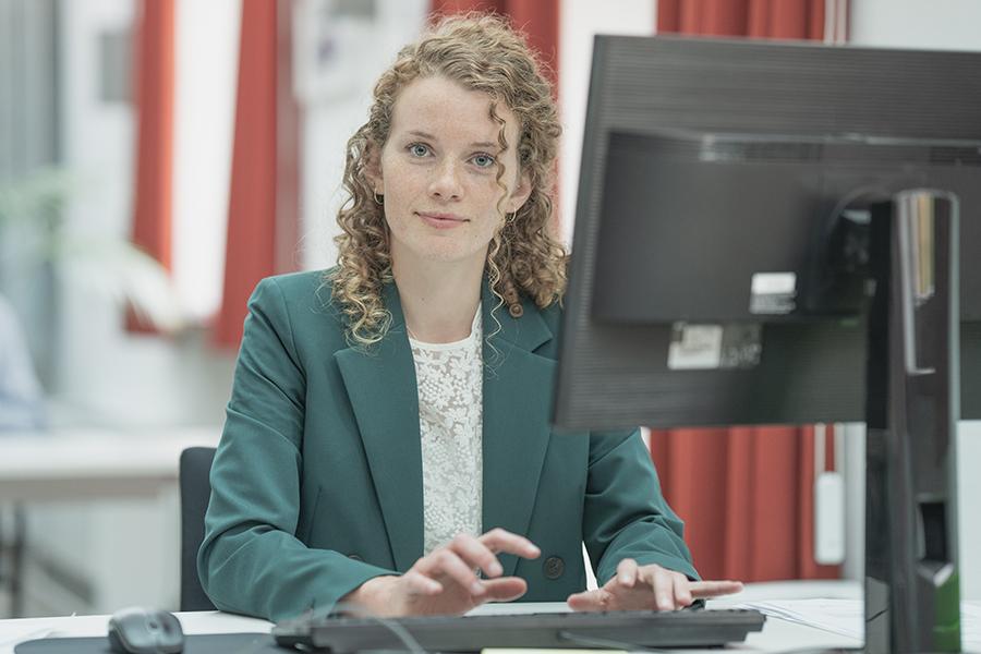 Eine junge Frau mit hellen lockigen Haaren sitzt vor einem PC.