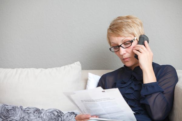 Eine Frau schaut auf Ihren Rentenbescheid und hält ein Telefon am Ohr. Eine Frau schaut auf Ihren Rentenbescheid und hält ein Telefon am Ohr.