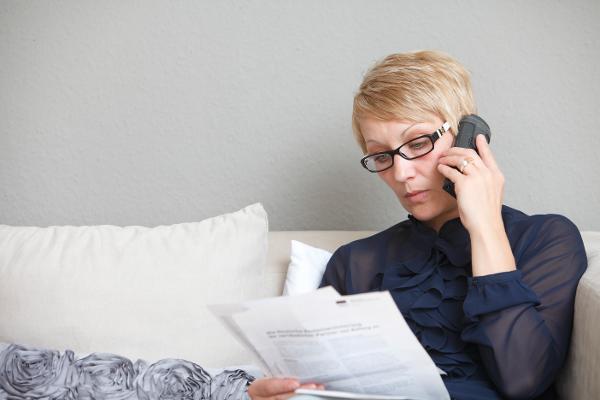 Eine Frau schaut auf Ihren Rentenbescheid und hält ein Telefon am Ohr.