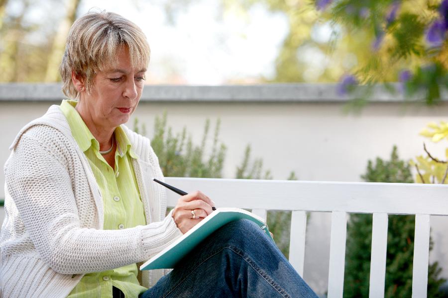 Eine Frau sitzt auf einer Bank und schreibt in ein Heft.