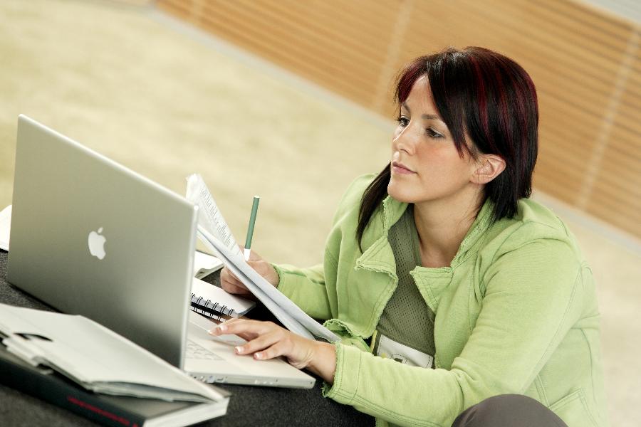 Eine Frau hält Informationsmaterial in den Händen und bedient einen Laptop Eine Frau hält Informationsmaterial in den Händen und bedient einen Laptop