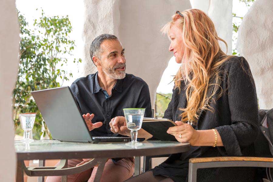 Ein Mann und eine Frau sitzen an einem Laptop und sprechen miteinander, sie hält ein Tablet Ein Mann und eine Frau sitzen an einem Laptop und sprechen miteinander, sie hält ein Tablet