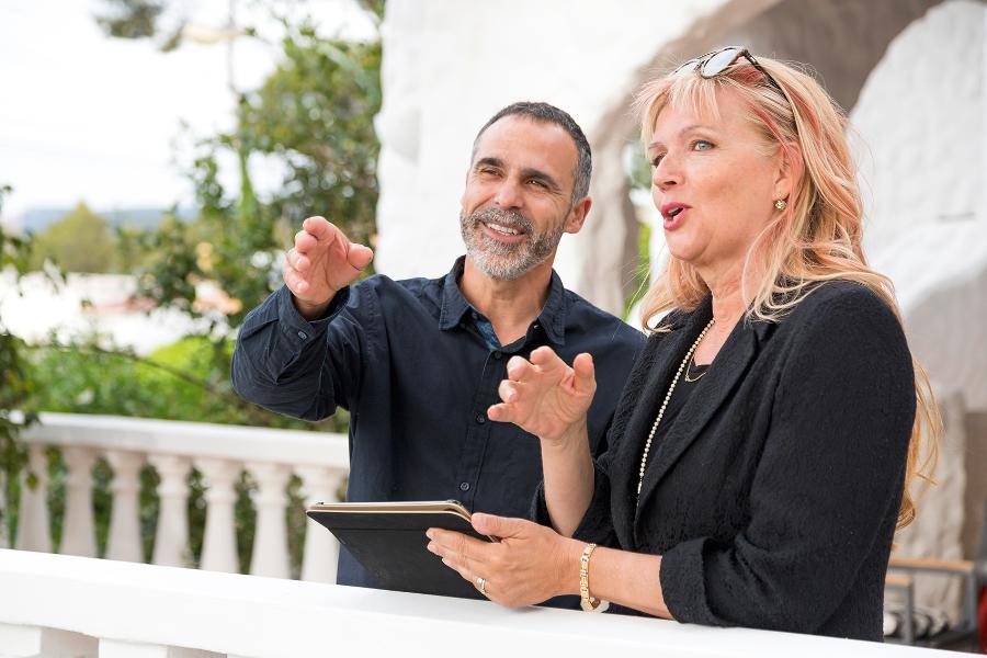 Ein Mann und eine Frau stehen an einem Geländer und sprechen, sie hält ein Tablet, er zeigt auf etwas in der Ferne Ein Mann und eine Frau stehen an einem Geländer und sprechen, sie hält ein Tablet, er zeigt auf etwas in der Ferne