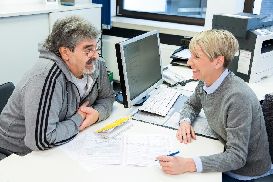 Ein Mann lässt sich von einer Mitarbeiterin bei der Antragstellung beraten Ein Mann lässt sich von einer Mitarbeiterin bei der Antragstellung beraten