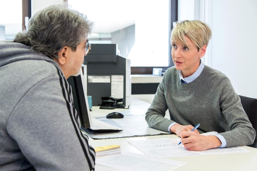 Ein Mann lässt sich von einer Mitarbeiterin bei der Antragstellung beraten Ein Mann lässt sich von einer Mitarbeiterin bei der Antragstellung beraten