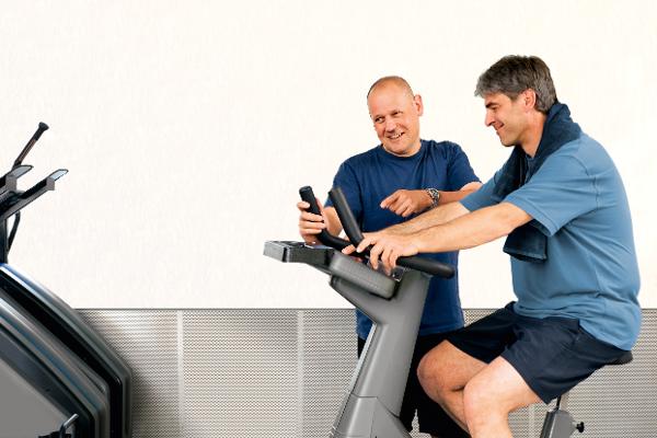 Ein Mann trainiert an einem Fitnessgerät und wird von einem Trainer betreut Ein Mann trainiert an einem Fitnessgerät und wird von einem Trainer betreut
