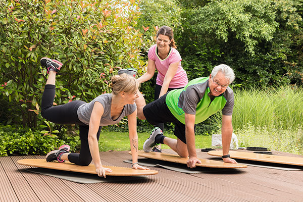 Eine Frau und ein Mann trainieren unter Anleitung auf einer Matte im Garten Eine Frau und ein Mann trainieren unter Anleitung auf einer Matte im Garten