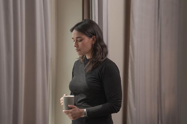 In schwarz gekleidete Frau steht mit einer Tasse Tee traurig am Fenster In schwarz gekleidete Frau steht mit einer Tasse Tee traurig am Fenster