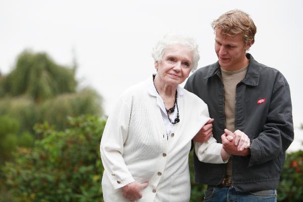 Ein junger Mann stützt eine Seniorin beim Laufen