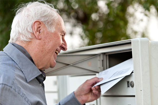 Älterer Herr steht an seinem Briefkasten und holt Post heraus Älterer Herr steht an seinem Briefkasten und holt Post heraus