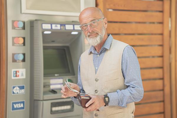 Älterer Herr steht vor Geldautomat und sortiert Bargeld in sein Portemonnaie