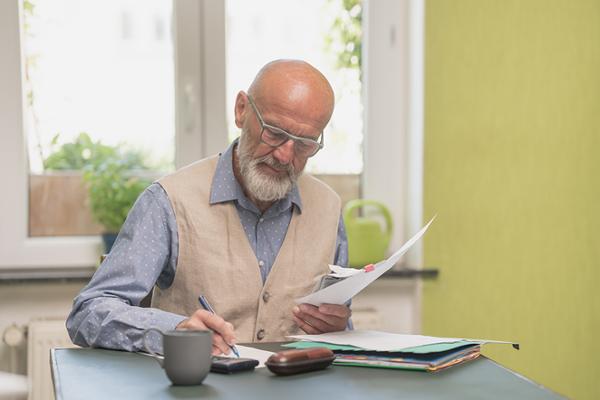 Älterer Herr mit Bart und Brille hält Unterlagen in der Hand, während er etwas notiert.