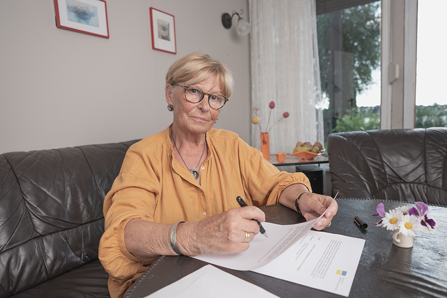 Ältere Dame sitzt am Wohnzimmertisch und füllt einen Antrag aus