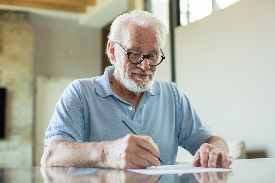 Ein älterer Mann sitzt an einem Tisch und füllt ein Formular aus. Ein älterer Mann sitzt an einem Tisch und füllt ein Formular aus.