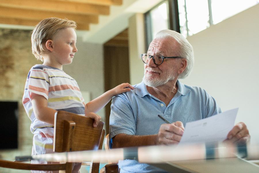 Ein Senior füllt ein Formular aus, sein Enkelsohn bzw. ein kleiner Junge guckt ihm dabei über die Schulter. Ein Senior füllt ein Formular aus, sein Enkelsohn bzw. ein kleiner Junge guckt ihm dabei über die Schulter.