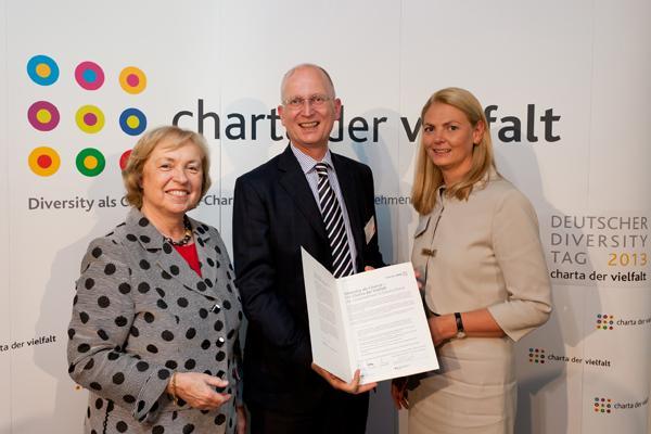 Das Bild zeigt Staatministerin Maria Böhmer, Direktor Volkart Steiner, der die Urkunde in der Hand hält, und Ana-Cristina Grohnert. Sie stehen vor einer Wand mit der Aufschrift Charta der Vielfalt.  