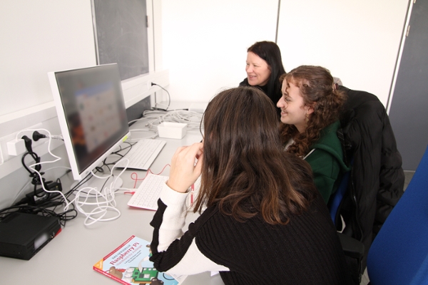Zwei Mädchen sitzen am PC. Eine Ausbilderin erklärt das Programm.